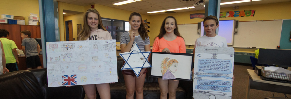 Three female students and 1 male student holding their book report projects