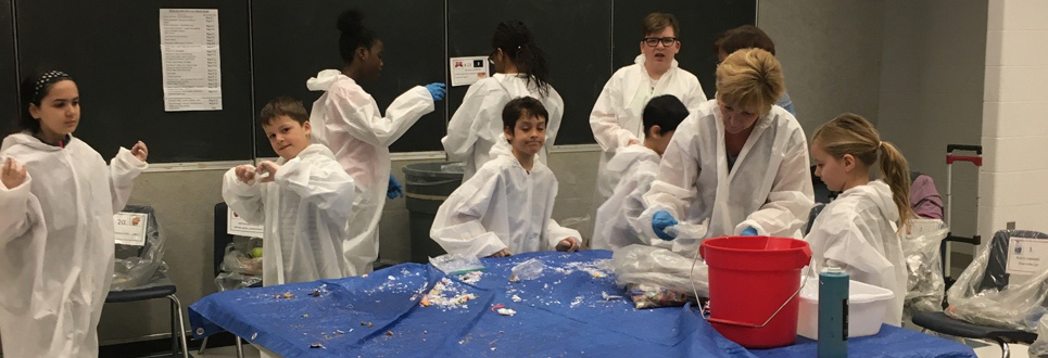 Students wearing white overalls and blue gloves doing a waste audit